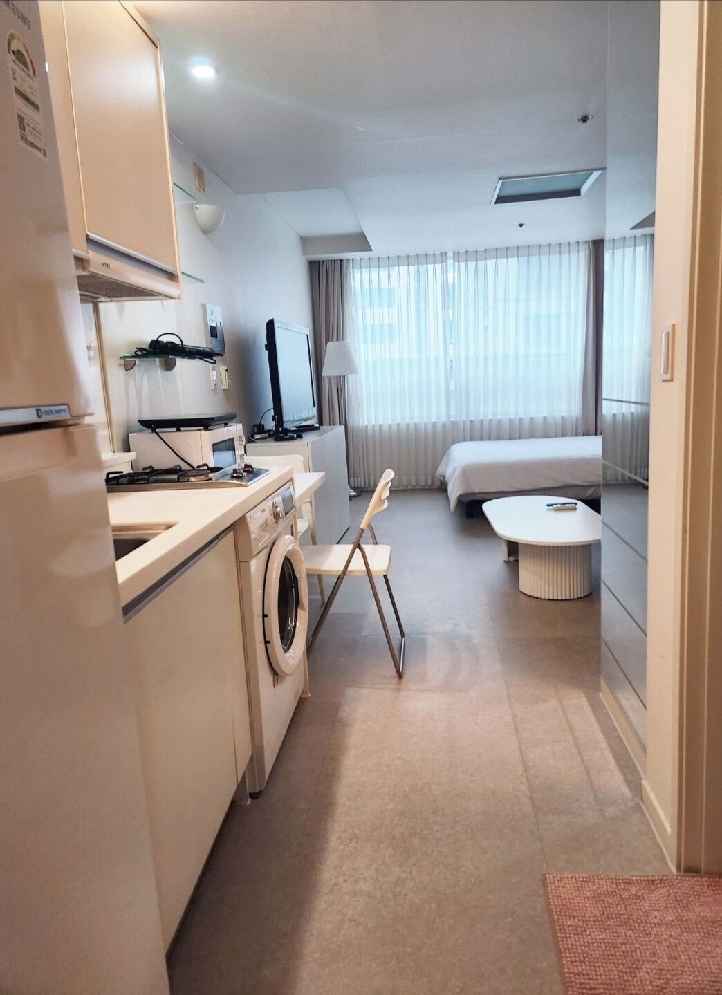 Una habitación de hotel compacta con kitchenette, una cama, una mesita pequeña y una silla.