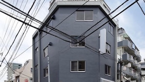 A multi-story building with a grey facade, multiple windows, and visible electrical wires. - TokyoPan B&B (Tokyo)