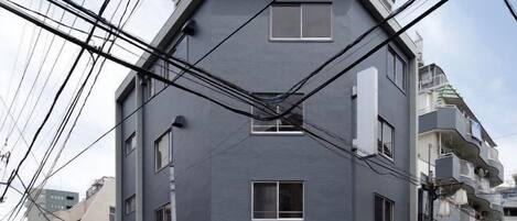 Un edificio de varios pisos con fachada plana, varias ventanas y cables eléctricos a la vista.