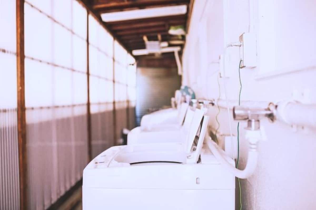 A row of white laundry machines in a hallway with metal walls and a wooden ceiling.