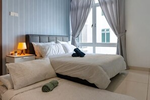 Una habitación de hotel con cama, mesita de noche con lámpara y ventana con cortinas.