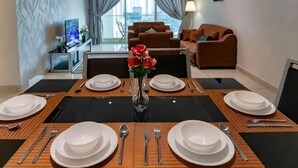 A dining area with a table set for four, a vase with flowers, and a view of a living room with a sofa and a TV. - A Chic 3BR KSL DEsplanade Residence, FREE Parking (Johor Bahru)