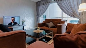 A modern living room with a sofa, a coffee table, and a television displaying a person. - A Chic 3BR KSL DEsplanade Residence, FREE Parking (Johor Bahru)