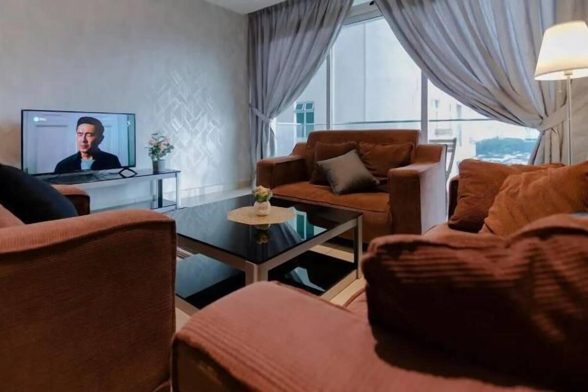 Un salon moderne avec un canapé, une table basse et un téléviseur qui diffuse une émission mettant en scène une personne.