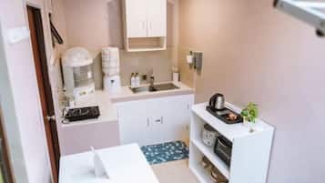 Una kitchenette compacta con cafetera, hervidor de agua y un lavamanos pequeño.