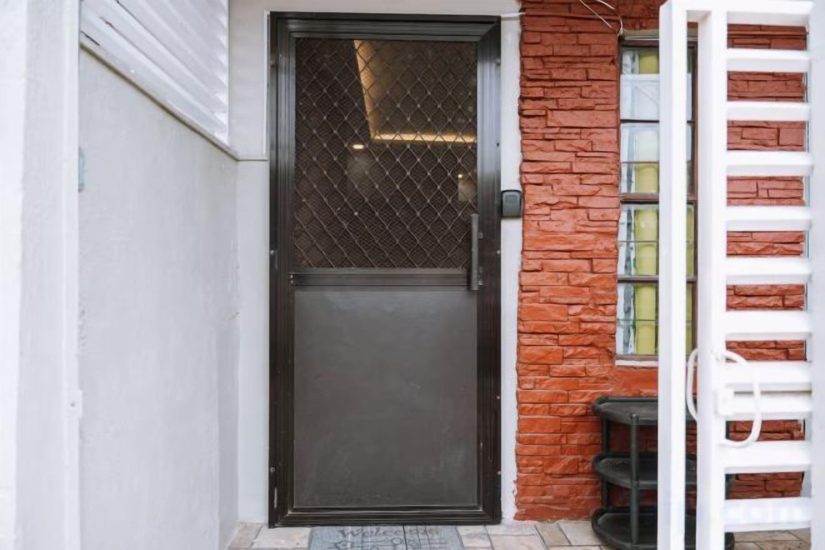 A closed door with a metal mesh window, a white doorbell, and a red brick wall.