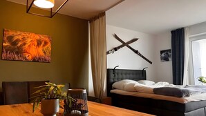 Una habitació amb un llit, una taula de dinar amb plantes, un quadre i una decoració de paret única.