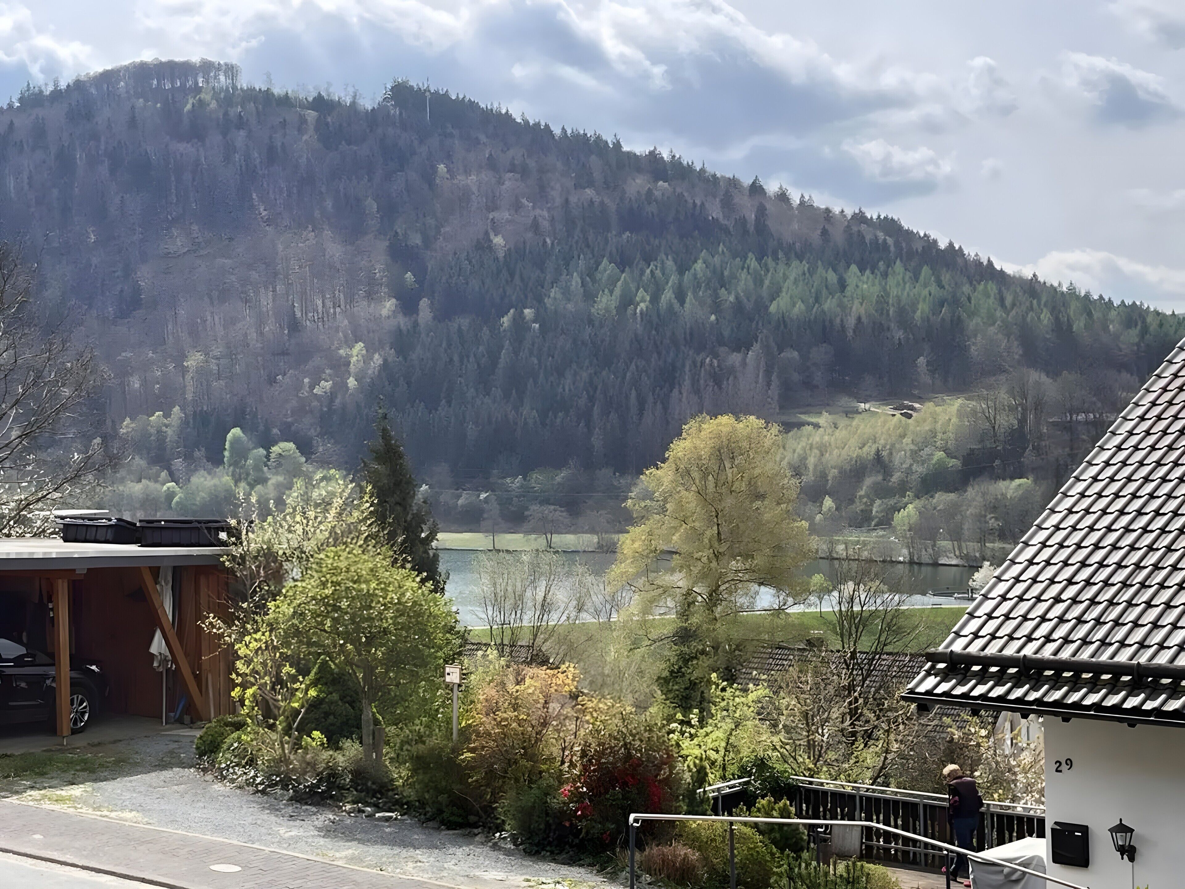 Ett hus med ett tak täckt av tegelpannor, ett garage och utsikt över en sjö och skogbeklädda berg.