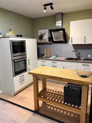 A modern kitchen with white cabinets, a wooden table, and a built-in oven.