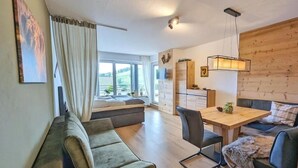 Un saló modern amb un sofà, taula de dinar i cadirees, una finestra gran amb cortines i una paret de fusta.