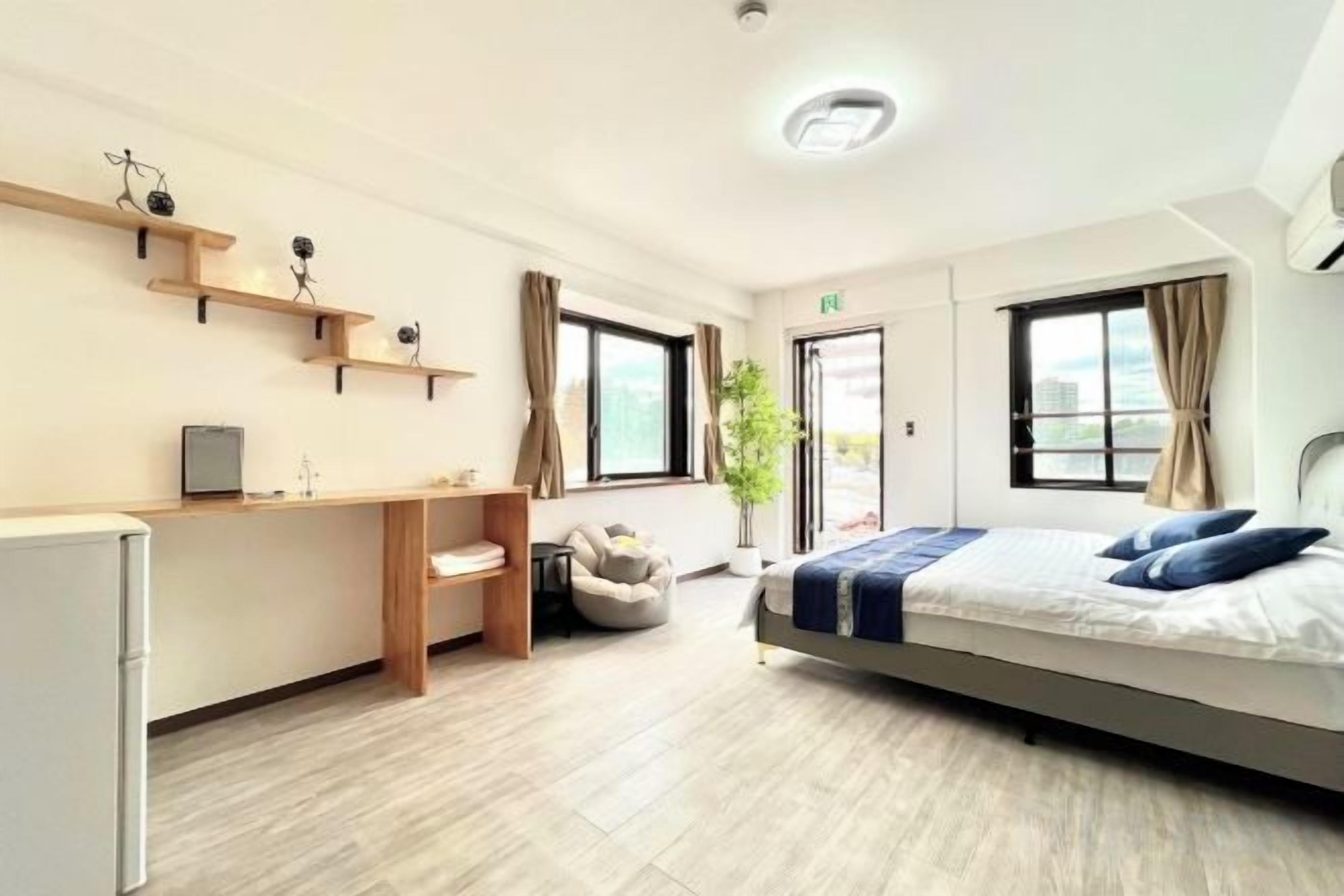 A modern hotel room with a bed, desk, chair, and a small kitchenette.