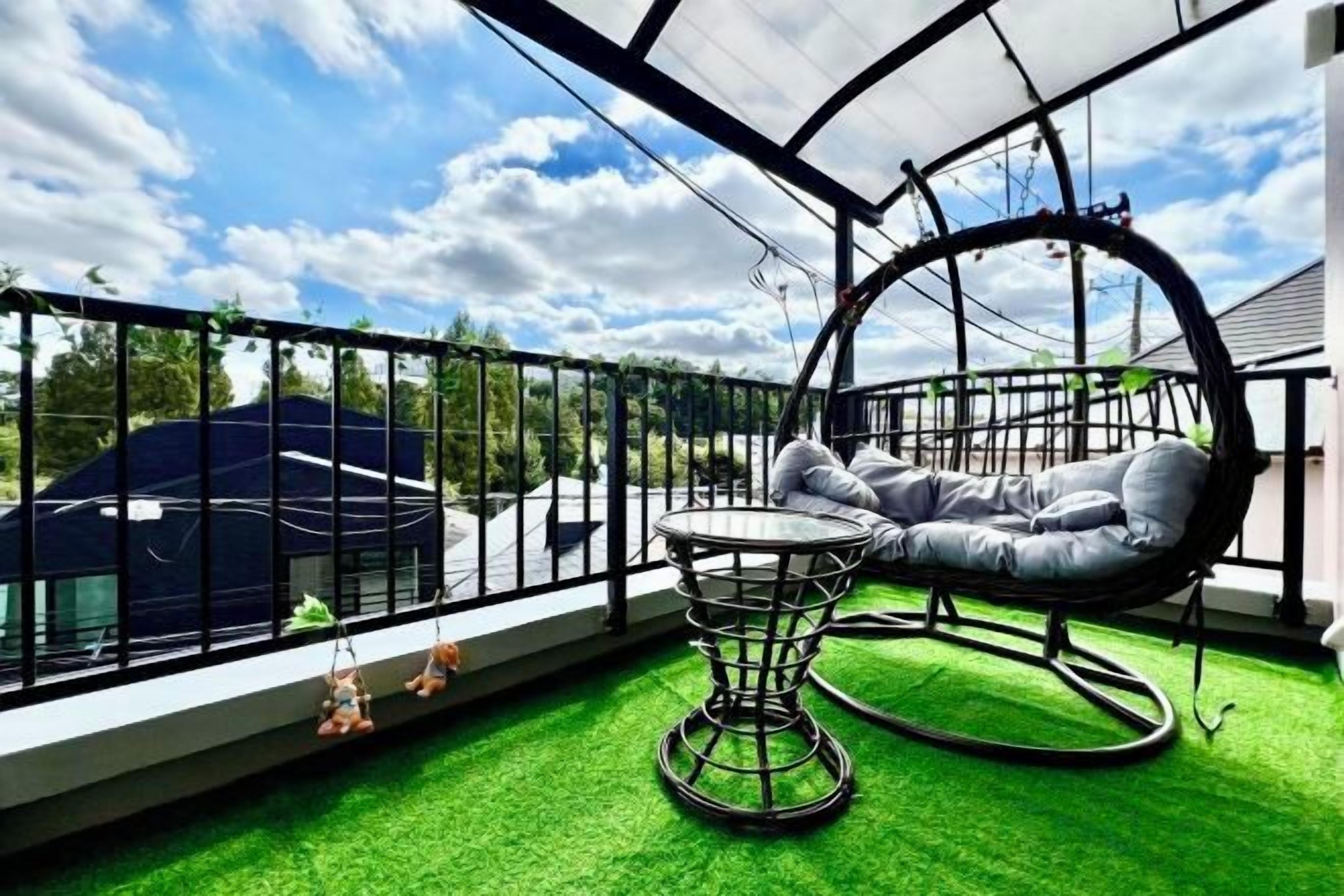 A balcony with a hanging chair, a small table, and a view of a car and trees.