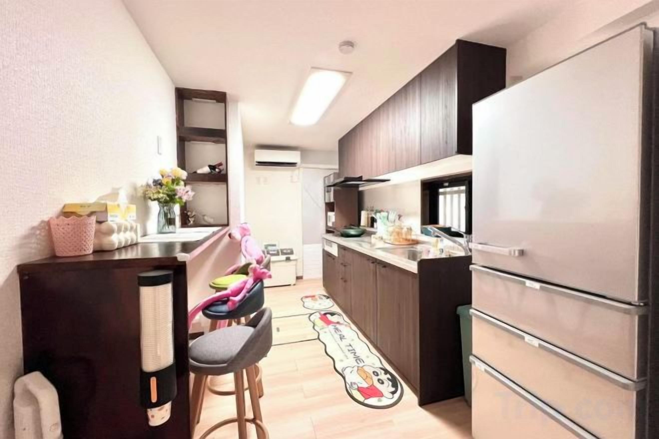 A compact kitchen with a refrigerator, a sink, and a countertop. There are stools and a small table.