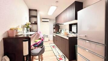 A compact kitchen with a refrigerator, a sink, and a countertop. There are stools and a small table.