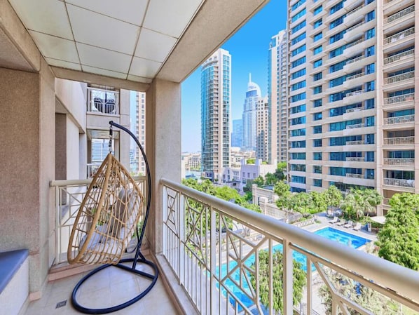 A balcony with a hanging chair, a pool, and high-rise buildings in the background.