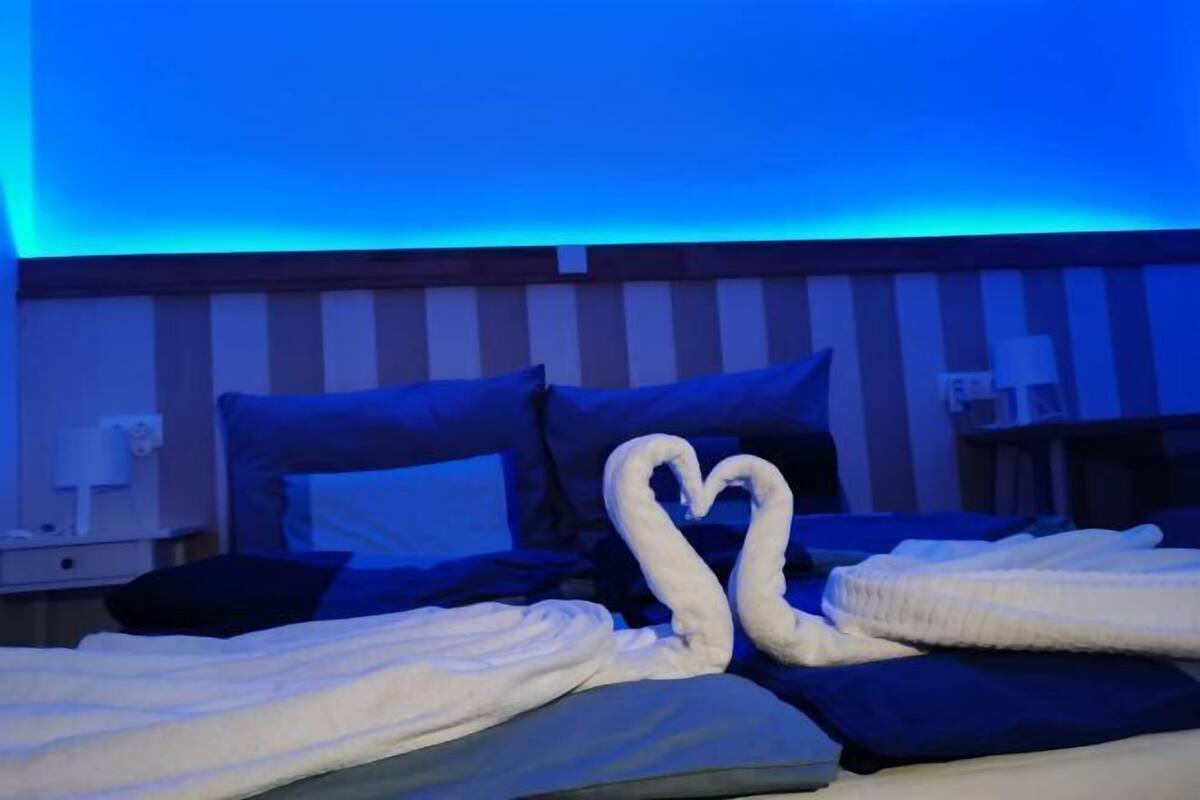 Habitació d'hotel amb parets a ratlles, un llit amb una tovallola decorativa amb forma de cor i una tauleta de nit amb una làmpada.