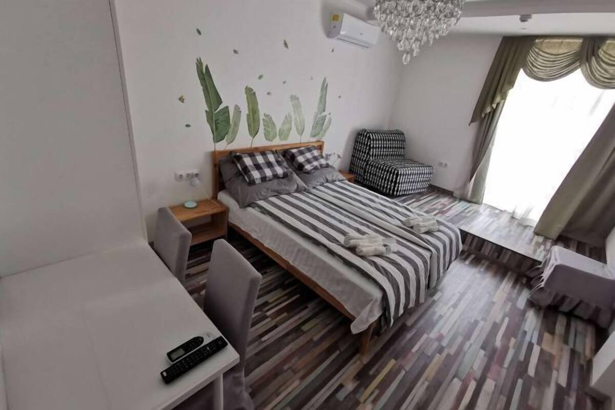 Habitació d'hotel amb llit, escriptori, cadira, taula petita, paret decorativa i finestra amb cortines.