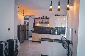 A modern kitchen with white cabinets, a black countertop, and a built-in microwave. There are three pendant lights hanging above the counter. - La Vie by Mar (Negombo)