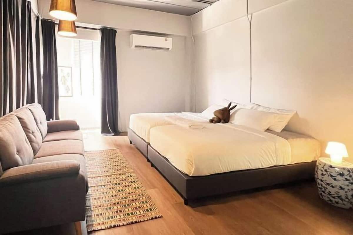 A modern bedroom with a bed, a sofa, a bedside table with a lamp, and a window with curtains.