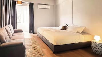 A modern bedroom with a bed, a sofa, a bedside table with a lamp, and a window with curtains.