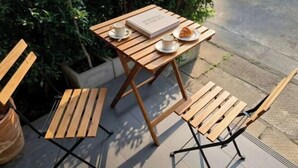 Une table en bois et deux chaises sur une terrasse, avec un livre et un croissant posés sur la table.