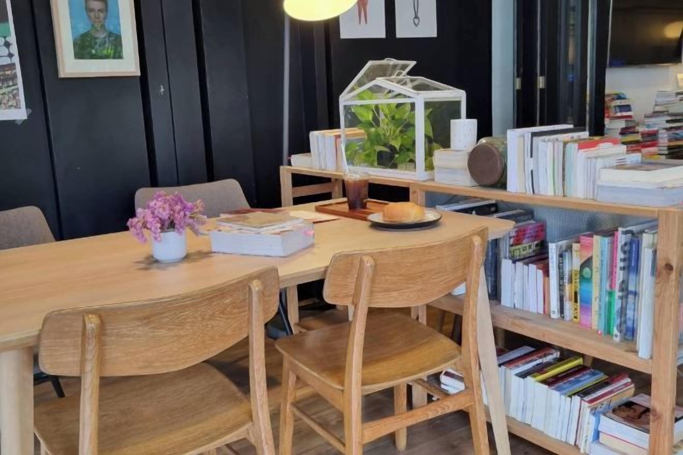 Une table à manger en bois avec des chaises, une bibliothèque remplie de livres, une petite plante et un objet décoratif posé sur la table.