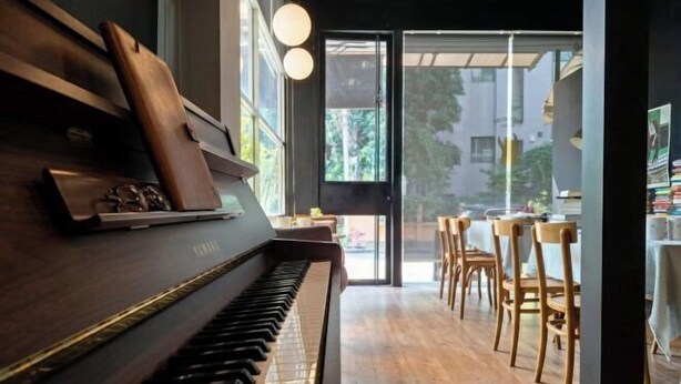 Un piano dans une pièce dont le sol est en bois, avec une vue sur l’extérieur à travers une porte vitrée.