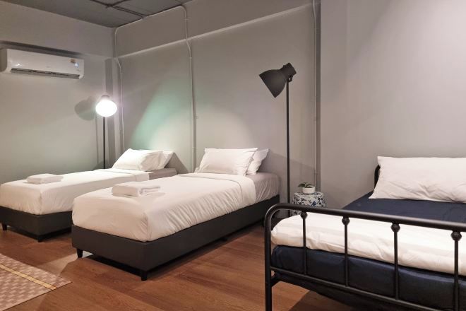 A hotel room with two beds, a bedside table, a lamp, and an air conditioning unit.