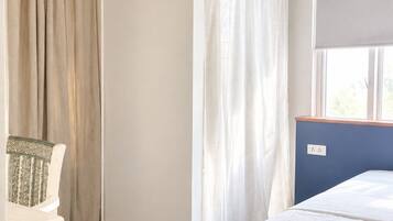 A room with a bed, a chair, a window with curtains, and a wall socket.