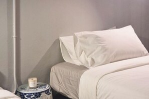 A bedroom with a bed, a bedside table with a candle, and a wall-mounted pipe. - Human Touch Room – Soulful Bangkok Hideout (Bangkok)