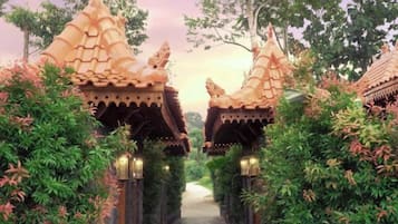 Un camí que condueix a edificis d'estil tradicional amb teulades ornamentades, envoltat de vegetació exuberanta.
