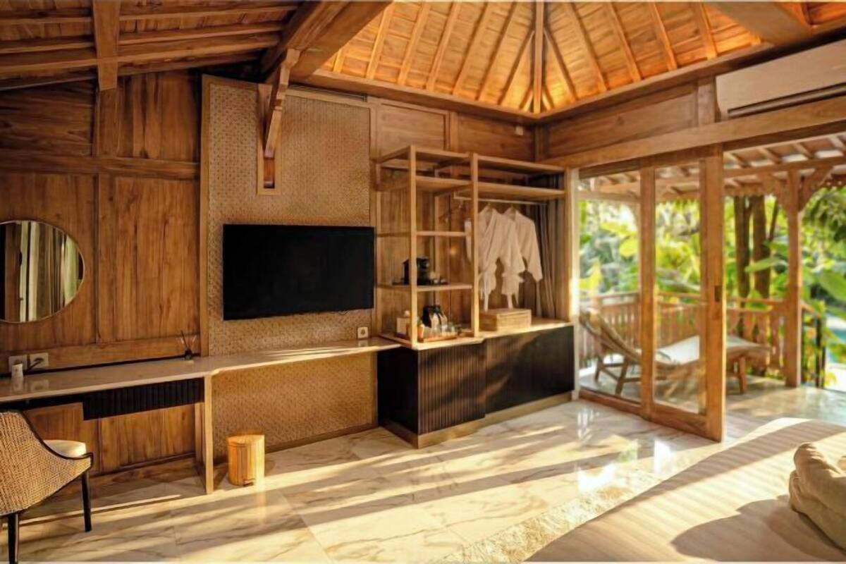 Un intérieur en bois avec une télévision, une étagère avec des vêtements et une vue sur la verdure à l’extérieur.