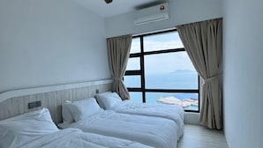 A hotel room with two beds, a large window with curtains, and an air conditioning unit. - JESSELTON QUAY BY KC SUITE (Kota Kinabalu)