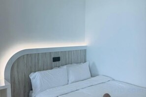 Una cama con ropa blanca y un cabecero con detalles en madera clara.