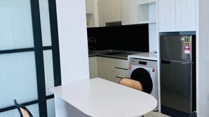 A compact kitchen with a washing machine, a refrigerator, and a dining area with a table and chair. - JESSELTON QUAY BY KC SUITE (Kota Kinabalu)