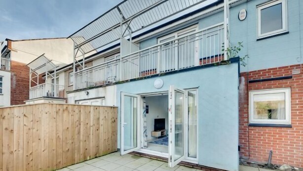 Un edificio residenziale con facciata blu, una recinzione in legno e un'ampia vetrata scorrevole che dà su un balcone.