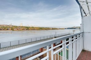 A river view from a balcony with a railing, a clear sky, and distant buildings.