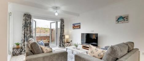 A living room with two grey sofas, a coffee table, a TV, and a balcony with curtains.