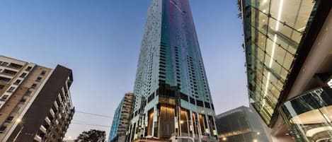 Een hoog gebouw met een moderne glazen gevel, gelegen in een stedelijke omgeving met andere gebouwen eromheen.