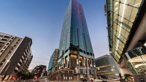 A modern high-rise building with a glass facade, surrounded by other contemporary buildings. - A Cozy Apt, Only a 5-min Walk to Victoria Market (Carlton)