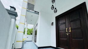 Un pasillo con una puerta de madera oscura, paredes blancas y suelo de baldosas.