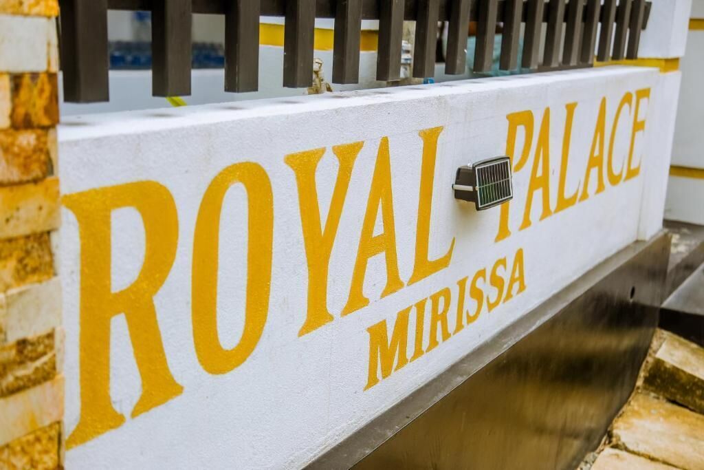 A sign with "ROYAL PALACE MIRISSA" written in large yellow letters on a white background.