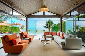 A modern living room with a large glass wall, a wooden ceiling, and a view of the ocean. - Baan Talay BeachFront Pool Villa B (Koh Samui)