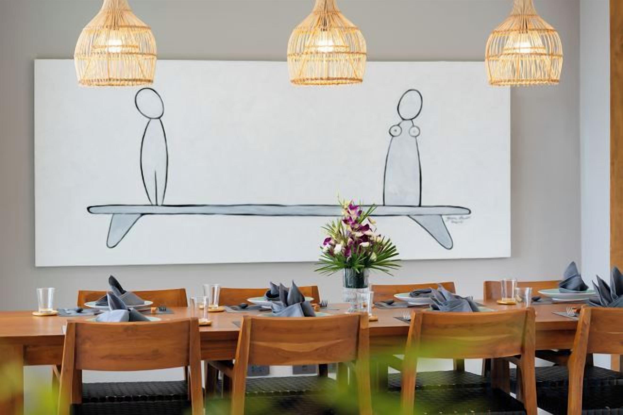 Un comedor con una mesa larga, sillas de madera y lámparas de mimbre colgantes.