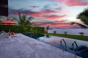 Ein Schwimmbad mit Blick auf das Meer und einen Sonnenuntergang.