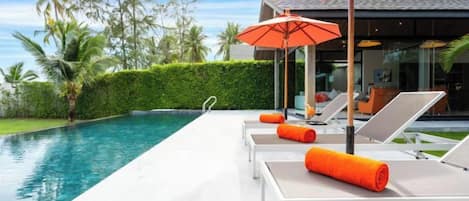 Área da piscina com espreguiçadeiras e um guarda-sol.