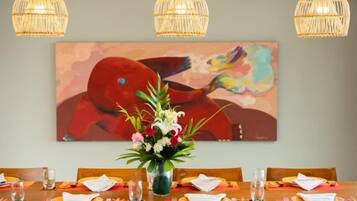 Un comedor con una mesa preparada para cuatro, un florero con flores y un cuadro abstracto y colorido en la pared.