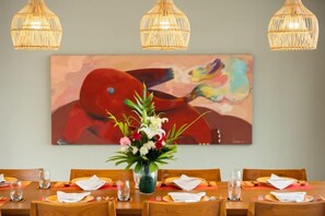 A dining area with a table set for four, a vase with flowers, and a colorful abstract painting on the wall. - Baan Talay BeachFront Pool Villa B (Koh Samui)