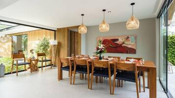 Un comedor con una larga mesa de madera, varias sillas, lámparas colgantes y un cuadro grande en la pared.