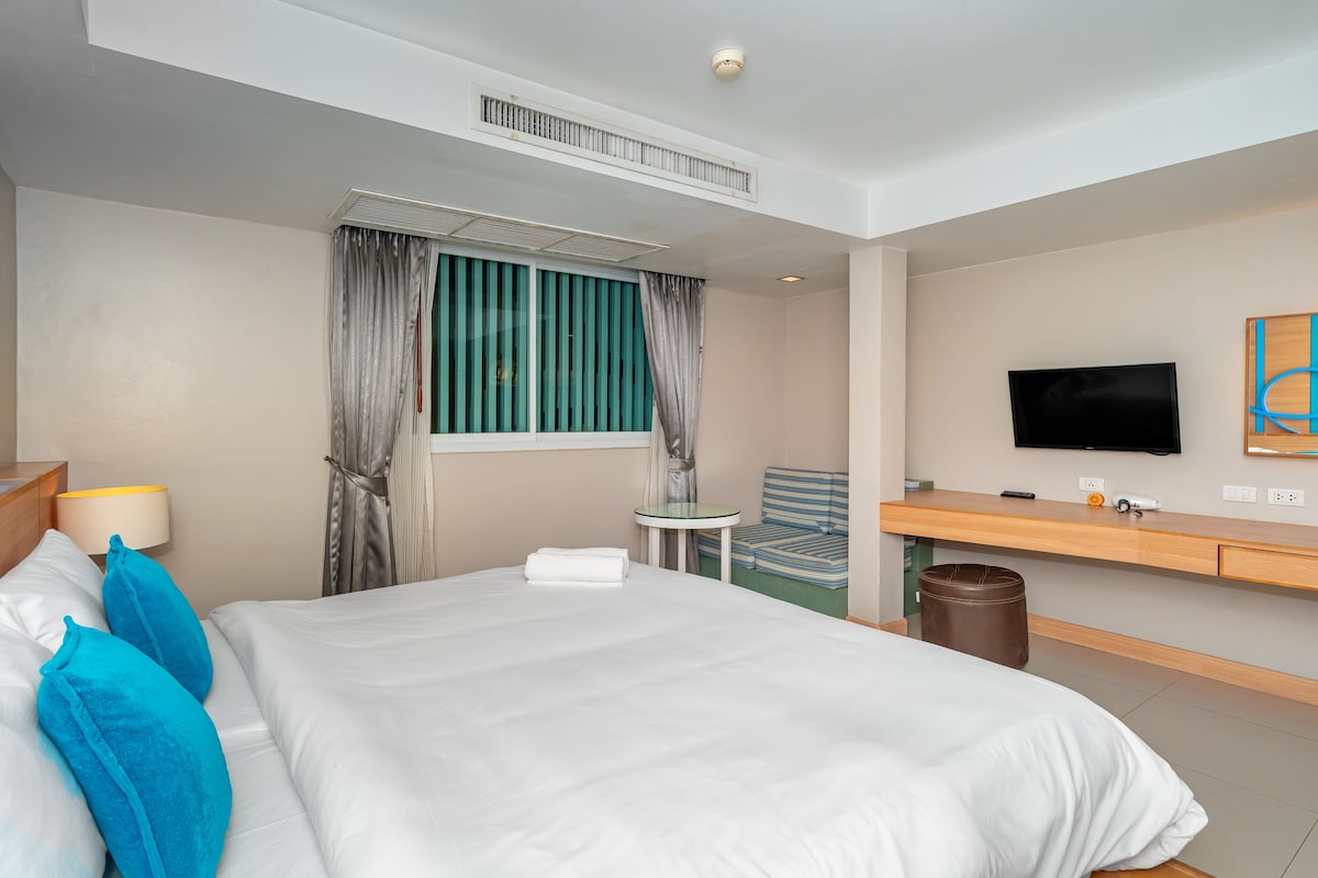 Una habitación de hotel con una cama, televisión, una mesita y una silla.